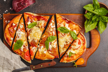 Oval homemade pizza with feta cheese, tomatoes and basil on a wooden board.