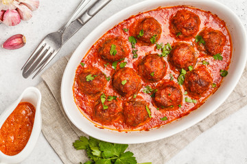Meatballs in tomato sauce with parsley in white dish, top view, copy space.