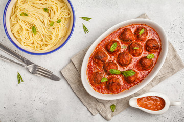 Pasta and meatballs in tomato sauce with basil in a white dish, top view.
