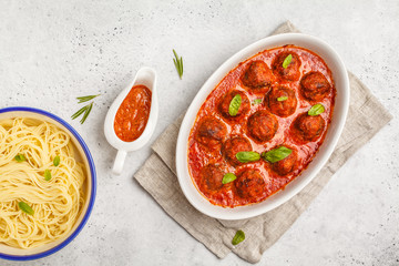 Pasta and meatballs in tomato sauce with basil in a white dish, top view.
