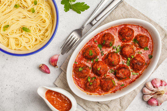 Pasta and meatballs in tomato sauce with basil in a white dish, top view.