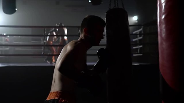 Guy in gloves beats a pear, in the background in the ring there is a sparring of kickboxers. Slow motion