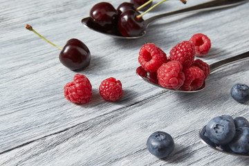 Sweet berriex mix on a gray background. Ripe blueberries, cherries, raspberries in a spoons.