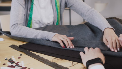Fototapeta premium Close-up of a hands of tailored fashion designers working with materials, they sitting at the beautiful atelier with different tailoring tools and clothes. Two tailors createn a new collection of