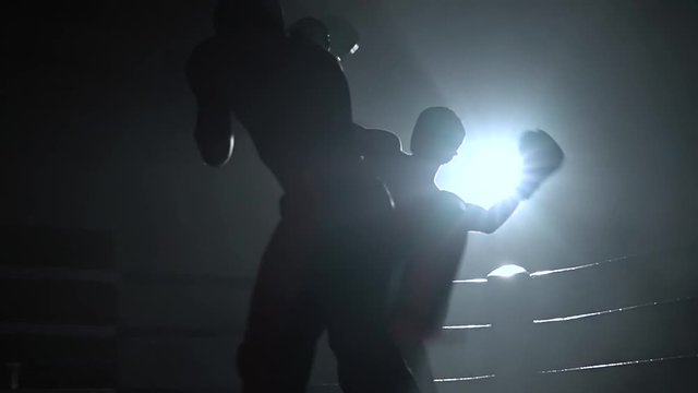 Two guys in helmets and boxing gloves to fight in the ring . Slow motion. Silhouette