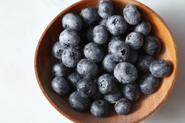 Ripe sweet blueberries in water droplets in the wooden plate on a gray background. Top view.