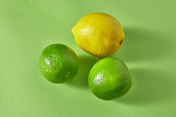 Organic natural ripe bright green limes and one yellow lemon on a green background.