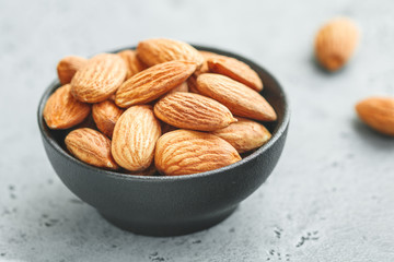 Fresh almond nuts in a back bowl on a textured grey table.