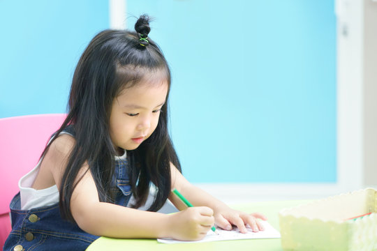 Asian children or kid girl and student happy smile and learning for coloring or paint on white paper with teacher at kindergarten classroom and nursery or pre school on colorful and blue background