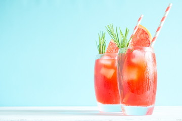 Refreshing cocktail of grapefruit with ice and rosemary on colored background of mint. Healthy citrus summer drink. 