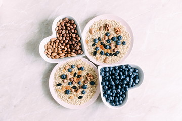 Ingredients for cooking healthy breakfast. Blueberries, nuts, oat flakes, dried fruits,raisins on a light marble table. Healthy food concept. Flat lay, top view, copy space 