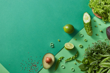 Freshly picked greens for salad - lettuce, green pea sticks, rosemary, avocado, lime, cucumber on a wooden brown board on duotone green background. Top view. Copy space.