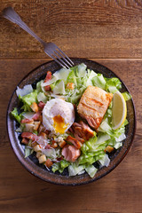 Salmon caesar salad. Crispy pan fried salmon fillet, bacon, poached egg, lettuce and croutons dressed with parmesan cheese. View from above, top studio shot