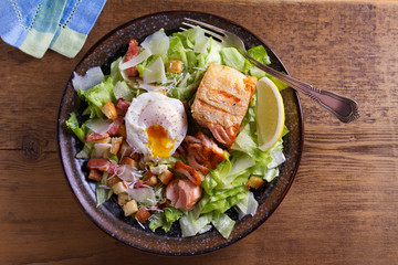 Salmon caesar salad. Crispy pan fried salmon fillet, bacon, poached egg, lettuce and croutons dressed with parmesan cheese. View from above, top studio shot