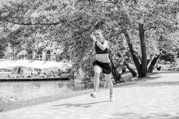 Beautiful brunette female fitness girl running, exercising outside in a leafy and green city park. Lady in sports top jogging in park. Healthy girl lifestyle background with copy space 