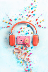 Headphones with a pink cassette tape with a tape of bubble gum in a gentle and sweet music concept with copy space. Candies, sprinkles, and marmalades in a pastel color flat lay with sweets