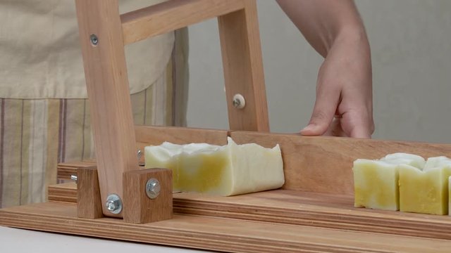 A close-up of woman's hands cutting the soap into bars on the soap-cutting machine. She puts all the bars in a row.