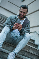 Love this song. Young man in headphones using his smartphone while sitting against industrial city vie