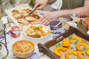 rice with pumpkin and honey on the table and other autumn food, pie with pear. Delicious family dinner in the courtyard. Men's hands cut the cake. Copy space