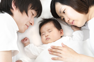 Obraz na płótnie Canvas 新生児と添い寝し見つめる若い夫婦、幸せな家族イメージ