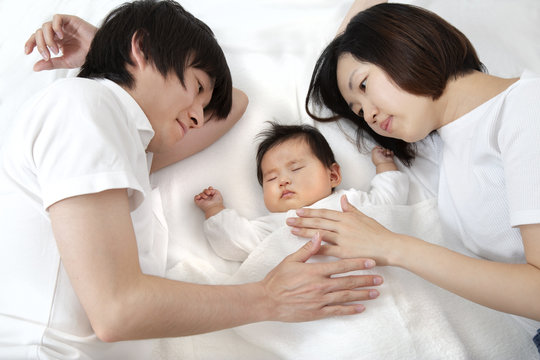 新生児と添い寝し見つめる若い夫婦、幸せな家族イメージ