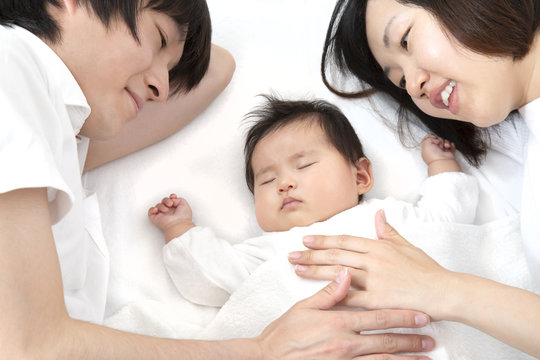 新生児と添い寝し見つめる若い夫婦、幸せな家族イメージ