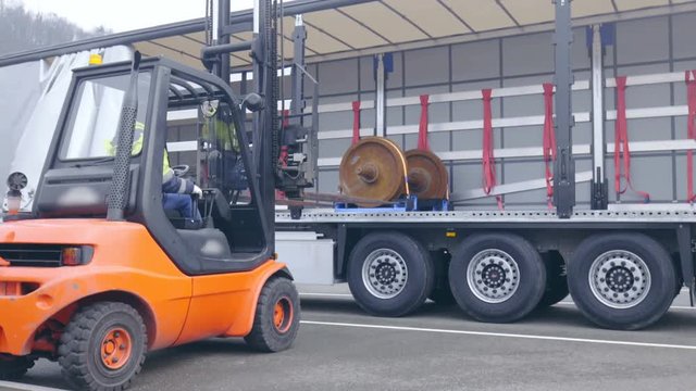 Forklift unloading cargo on a truck trailer wide shot 4K. Wide view of a forklift in focus driving back after unloading train wheelbases on big empty truck trailer.