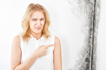 Wall fungus. Aspergillus. A beautiful girl in a white T-shirt points a finger at the black mold on...