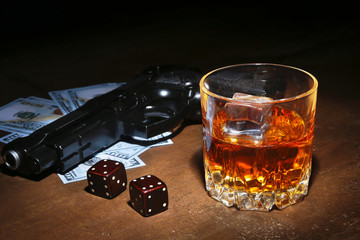Glass of whiskey or cognac, gun, playing cards with money on the black mirror table. The concept of criminal.