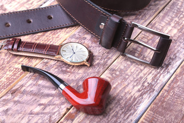 Set of men's accessories for the business with leather belt, wallet, watch and smoking pipe on a wooden background. The concept of fashion and travel.