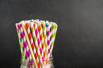 Different colors paper straws in glass jar on black background