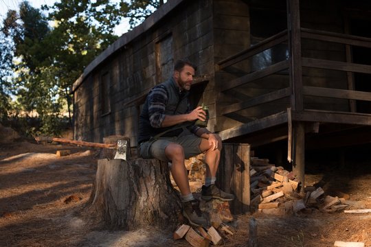 Man with water bottle sitting on tree stump outdoors
