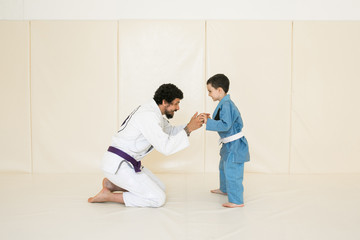 Male karate instructor training little child in dojo or jiu-jitsu at gym at tatami. Trainer teaches kid the basics of fighting for self-defense