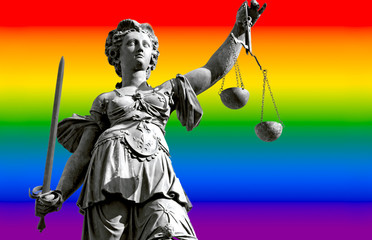 Die Gerechtigkeitsgöttin Justitia vor dem Hintergrund einer unscharfen Regenbogenfahne oder...