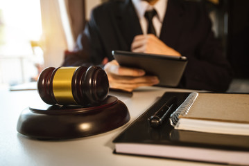 Justice and law concept.Male judge in a courtroom with the gavel,working with,digital tablet computer docking keyboard,eyeglasses,on wood table 