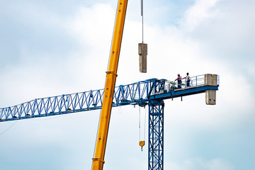Setting up a blue tower crane in the construction site. Workers are started to install the concrete...