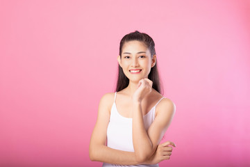 Portrait of a smiling attractive woman in white tanktop outfit posing while standing and smiling at camera isolated over pink background.