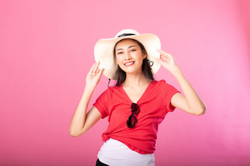 Fototapeta premium Portrait of a smiling attractive woman in summer outfit and hat posing while standing and looking at camera isolated over pink background.