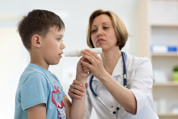 Little school boy blowing to peak metr medical device. Doctor examining child's lungs