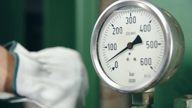 Pressure counter rising slowly close-up 4K. Dolly slide shot of pressure counter in focus with a hand of a worker wearing gloves in the background out of focus.
