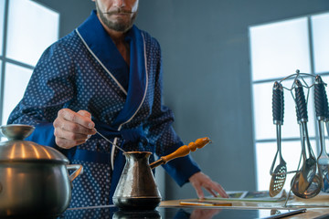 An elderly man is mixing a spoon of coffee in a brass turkey