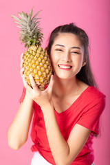 Attractive happy young woman holding fresh pineapple with a smile. Isolated over pink background. Summer lifestyle concept.