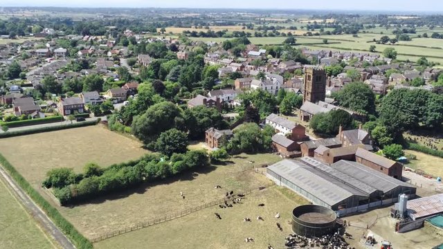 Aerial view, tilt up movement. Small city, town in UK, Sandstone church tower, farm 