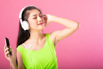 Portrait of a happy attractive woman in summer outfit listening  and dancing to music with her headphones isolated over pink background.