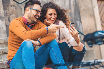 Young smiling couple using mobile phone while sitting on the stairs.