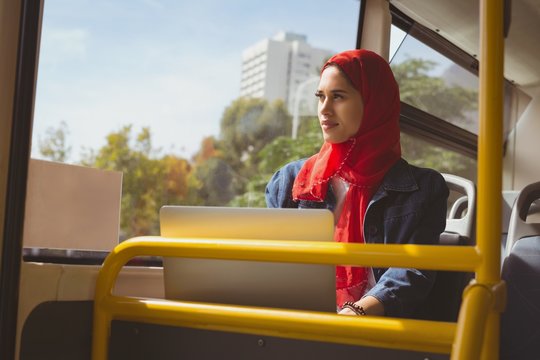 Young woman with laptop looking through window while travelling in bus