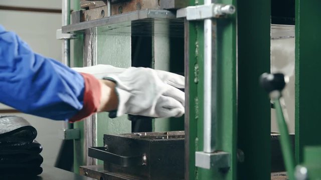 Worker add rubber material in to press machine 4K. Long shot dolly slide from right to left with refocusing from counter to press and back to worker's hand.
