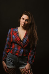 Fashionable young woman with long hair posing in checkered jacket on a dark studio background with shadows