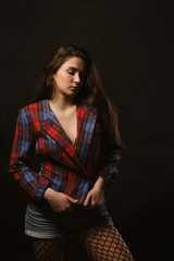 Fashionable young woman with long hair posing in checkered jacket on a dark studio background with shadows