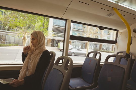 Hijab woman talking on digital tablet while travelling in bus